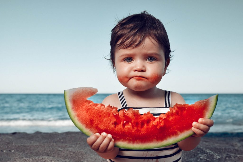 funny little girl on the beach eating watermelon