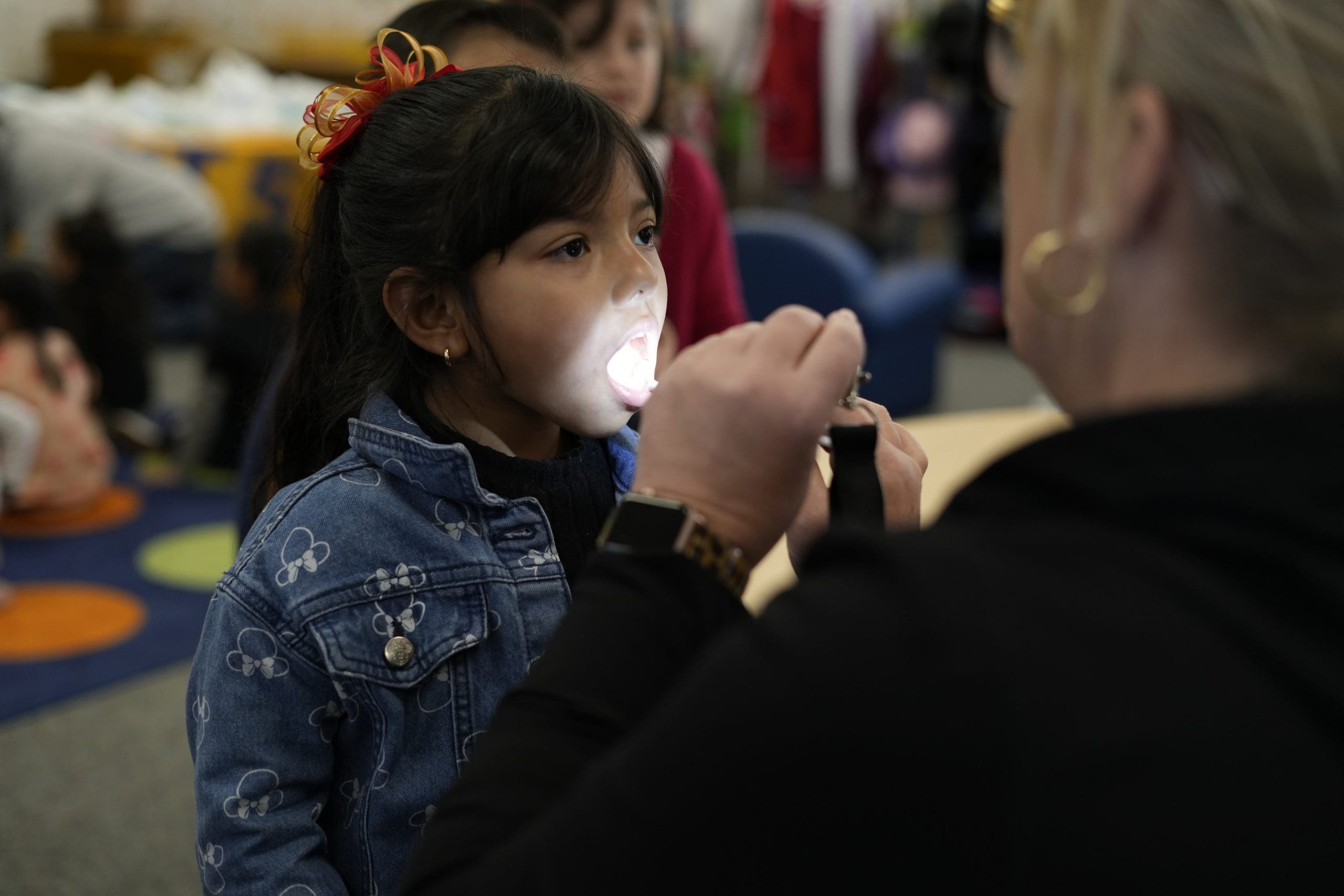 A woman flashing a light into a little girls mouth to assess her teeth.